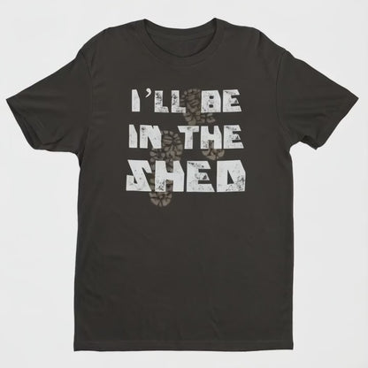 Black short-sleeved T-shirt featuring the humorous phrase 'I'll Be In The Shed' in bold white capital letters across the chest